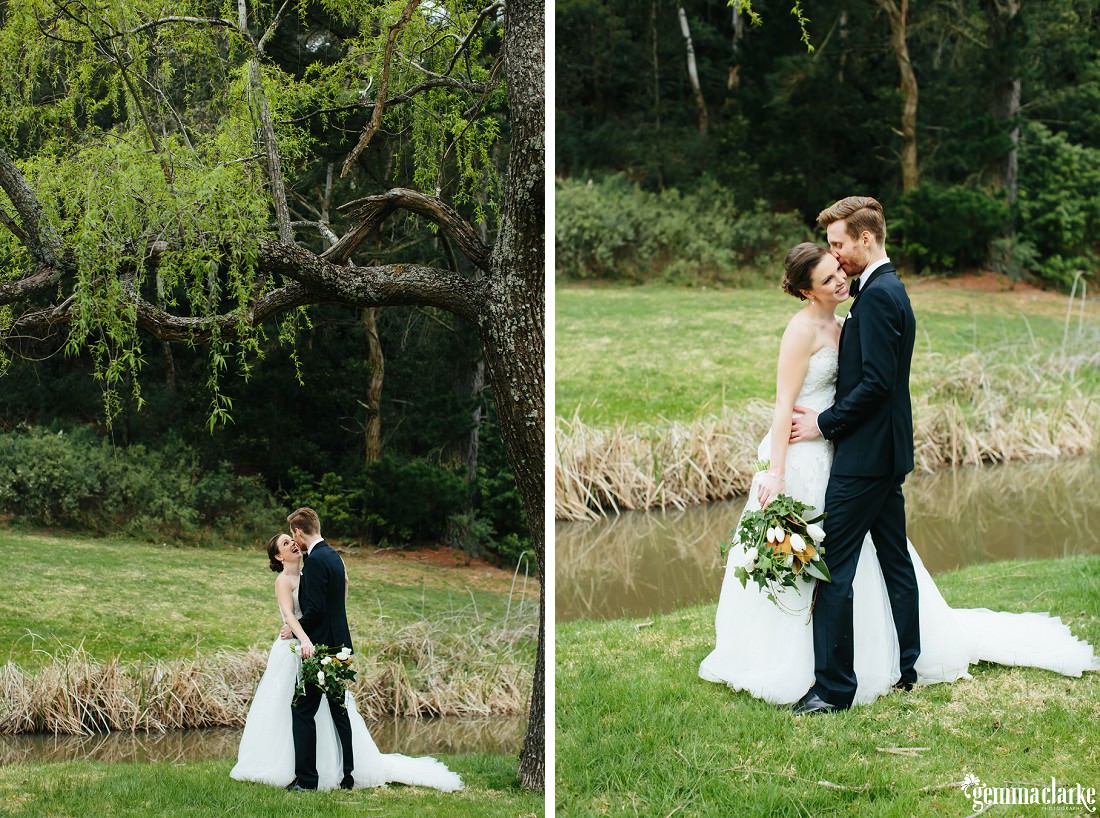 A bride and groom embrace under a tree beside a small lake