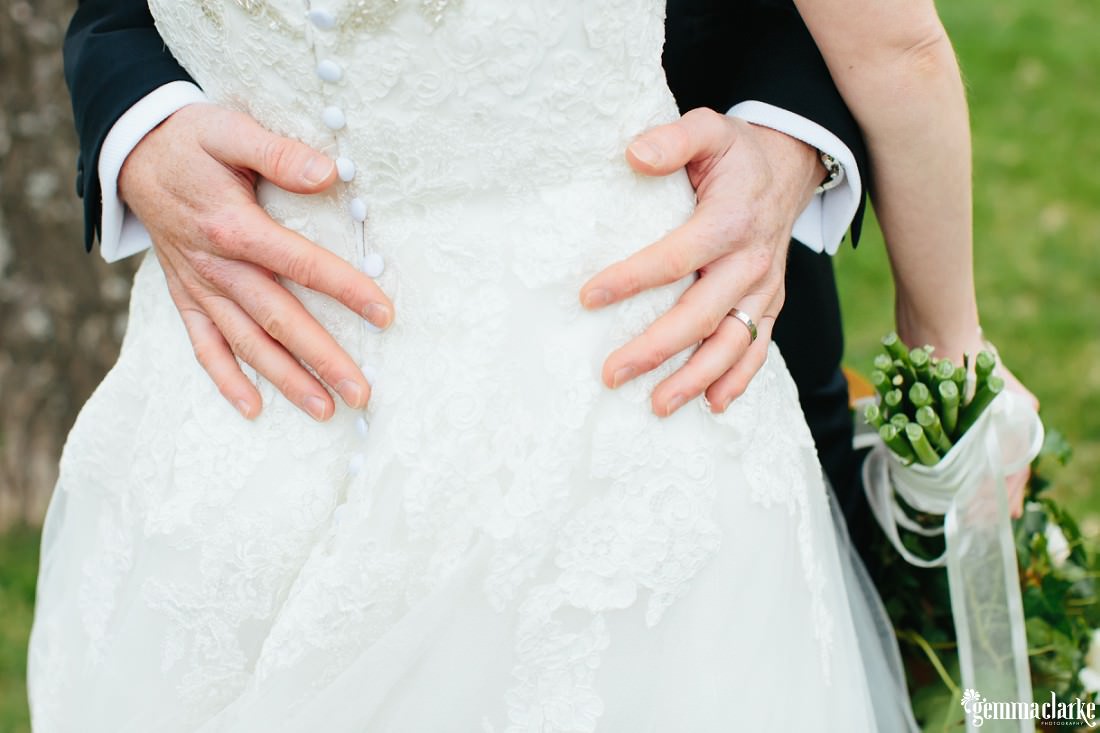 A close up of a bride's detailed dress as she is held close by her groom