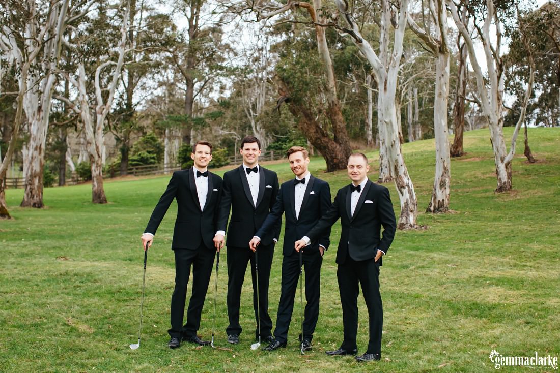 A groom and his groomsmen posing with golf clubs