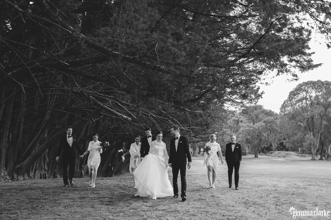 A bridal party walking along together beneath some large trees