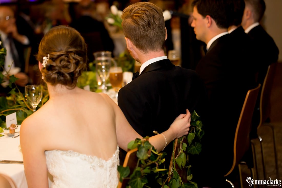 A bride with her arm around her groom while sitting at the bridal table at their reception