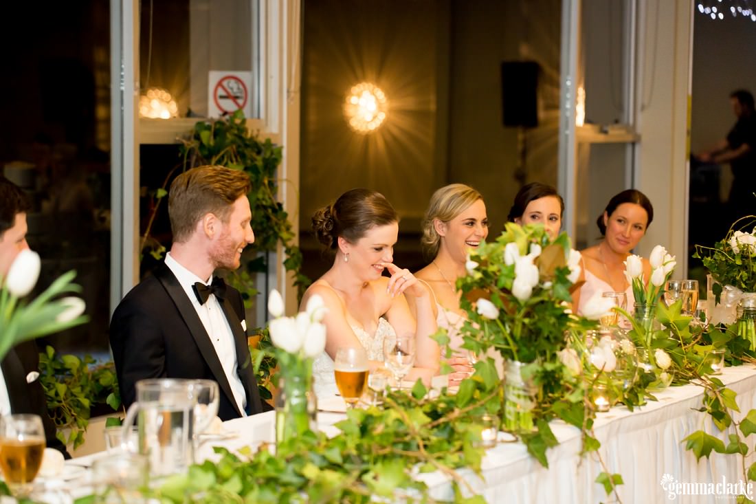 A bride and groom and some bridesmaids laughing at the bridal table