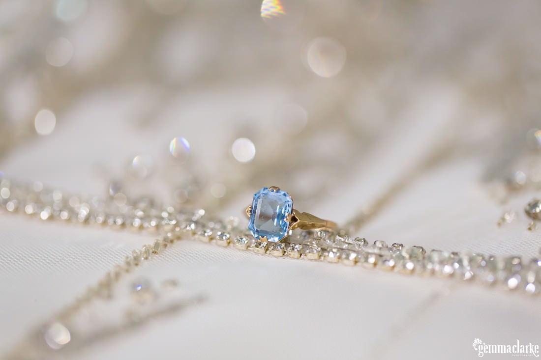 A close up of a ring laying on diamante details of a bridal gown