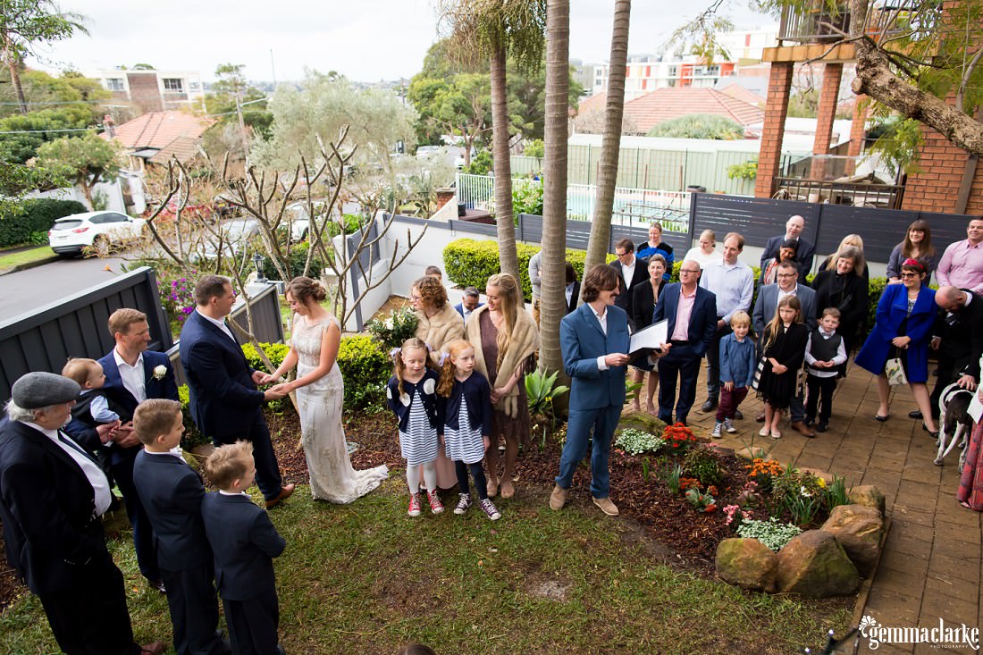 An above view of all the guests in the bride and groom's front yard gathered around listening to the ceremony as the bride and groom hold hands at this Wedding at Home