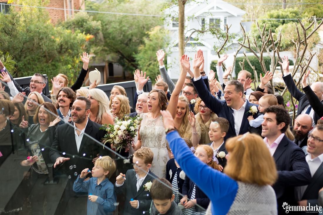 A group shot of a bride and groom and their wedding guests with their hands in the air