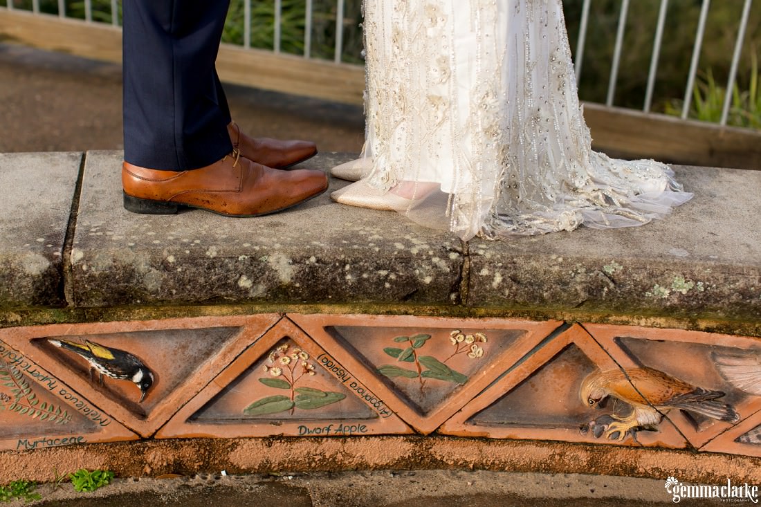 A close up of a bride and groom's shoes as they stand on a concrete structure at a lookout