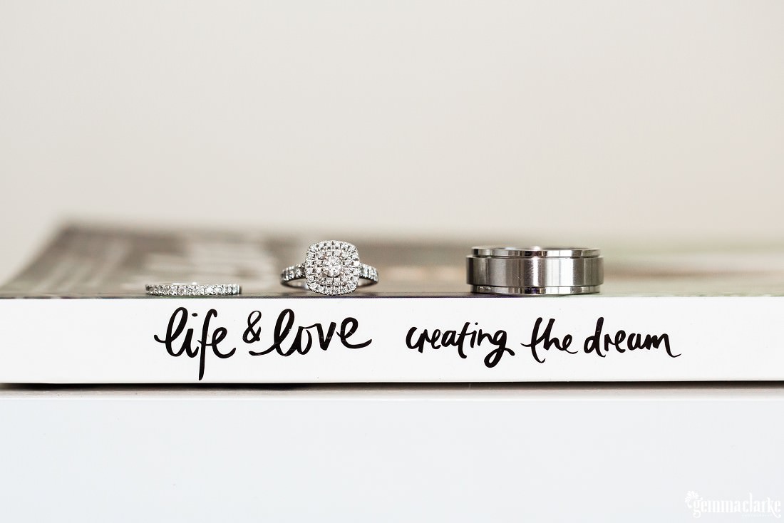 A man's wedding ring, a woman's wedding ring and engagement ring on a book titled "Life & Love, Creating the Dream"