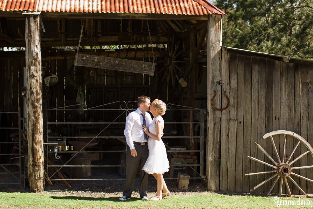A bride and groom kiss while standing in front of an old wooden farm building