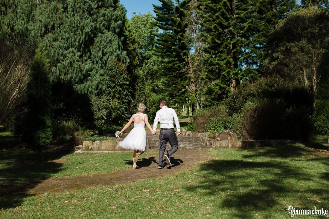 A bride and groom hold hands as they walk down a path through a garden