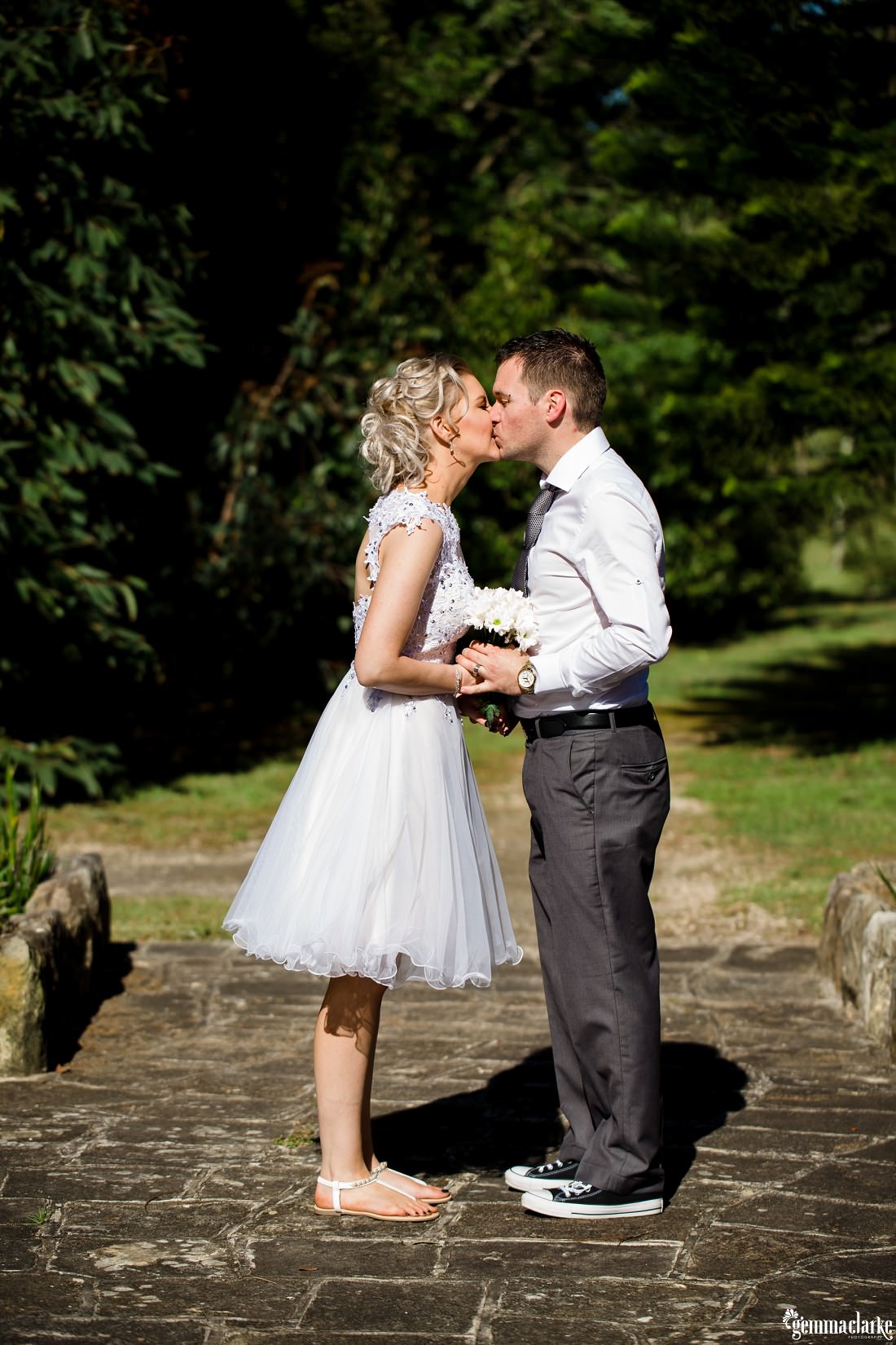 A bride and groom holding hands and kissing in a garden