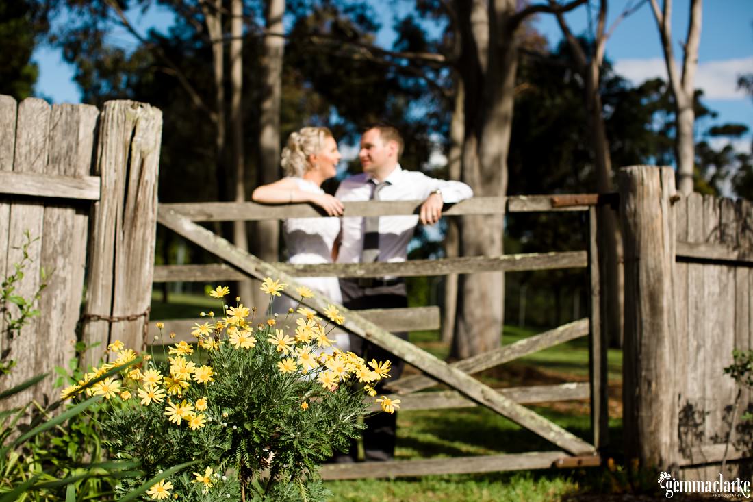 A smiling bride and groom leaning together on a wooden gate