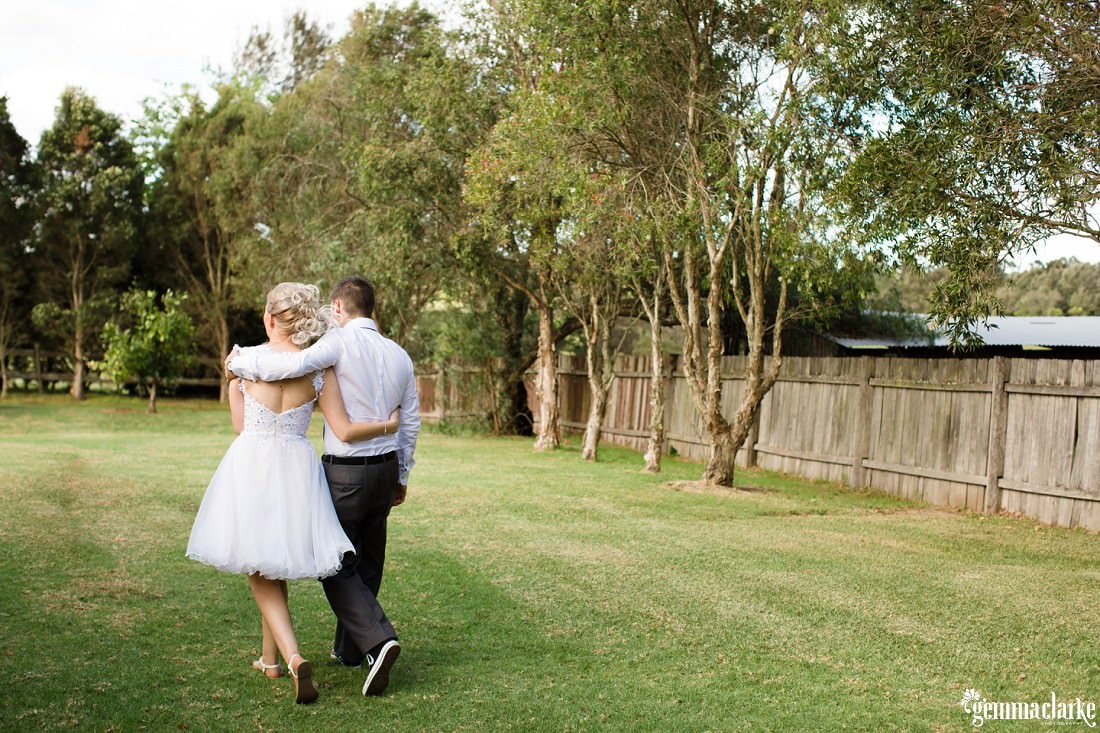 A bride and groom walking across the grass together arm in arm