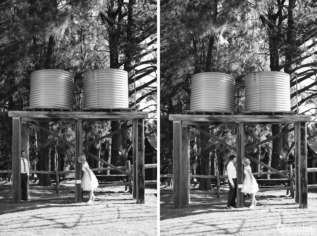 A bride and groom standing beneath a wooden structure with two corrugated iron tanks on top