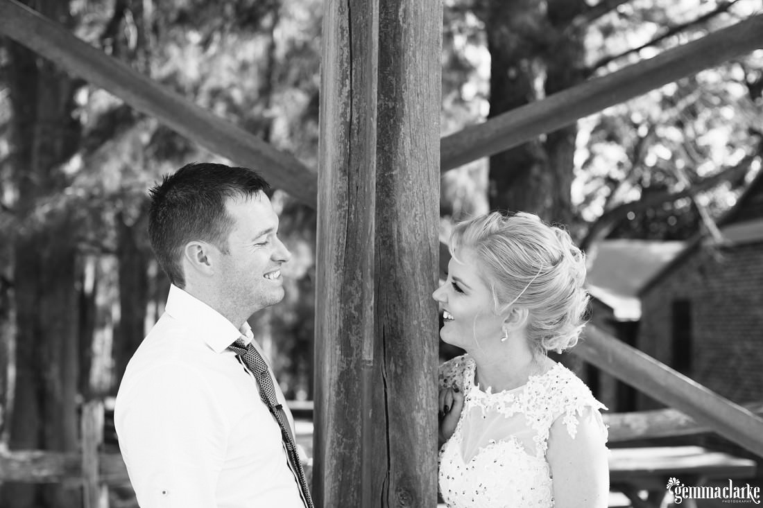 A bride and groom smile at each other from opposite sides of a wooden post