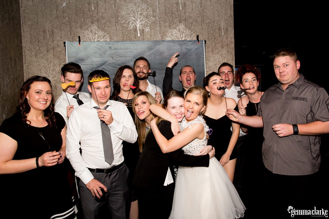 A bride and groom posing in a photo-booth with some of their guests