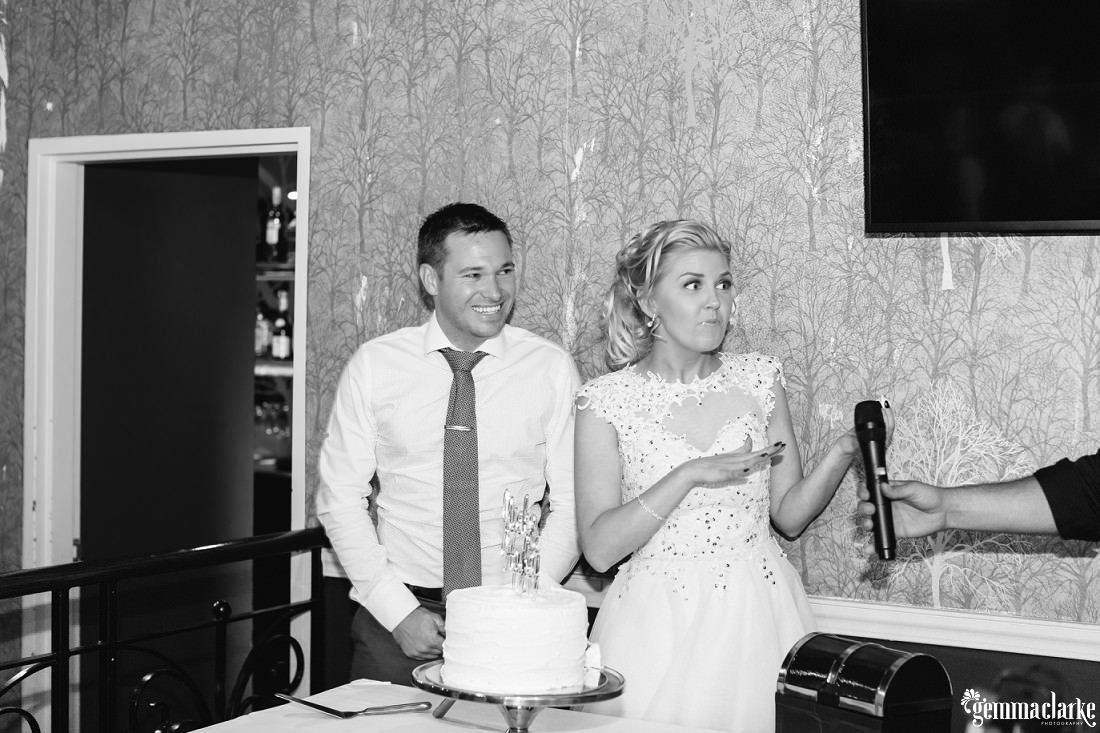 A bride being handed a microphone as her groom smiles behind her