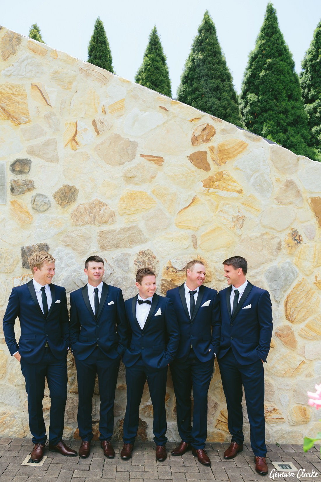 Groomsmen lined up in front of a beautiful sandstone wall with trees in the background at this Bendooley Estate Wedding