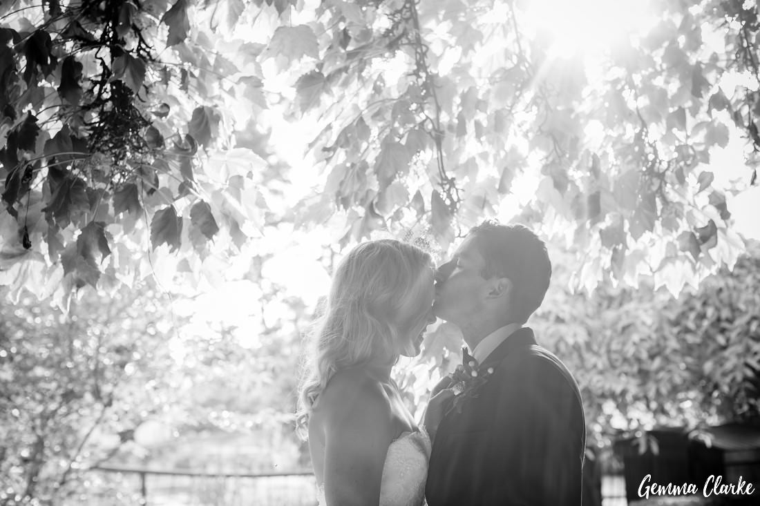 Sun flare added to this romance of this with the groom kissing the forehead of the bride and the overhanging leaves in the background at this Bendooley Estate Wedding