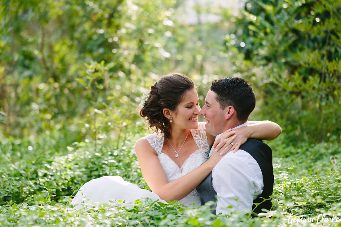 Bride and Groom snuggling with their arms around each other in the ground cover and it looks very romantic at this Belair Park Wedding
