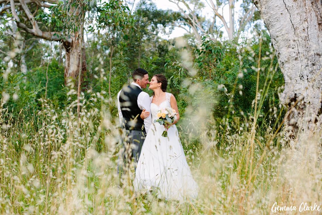 Bride and groom standing and cuddling on one side amongst the long grass at this Belair Park Wedding