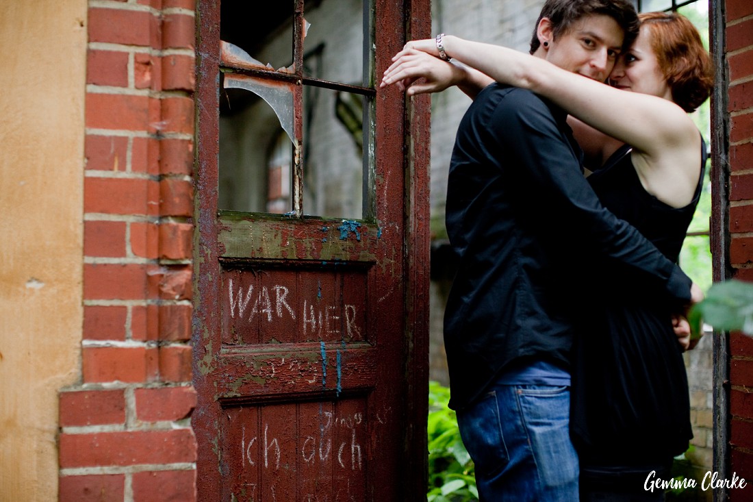 Couple snuggle in a broken doorway with graffiti on the doors in chalk in these Berlin Couple Portraits