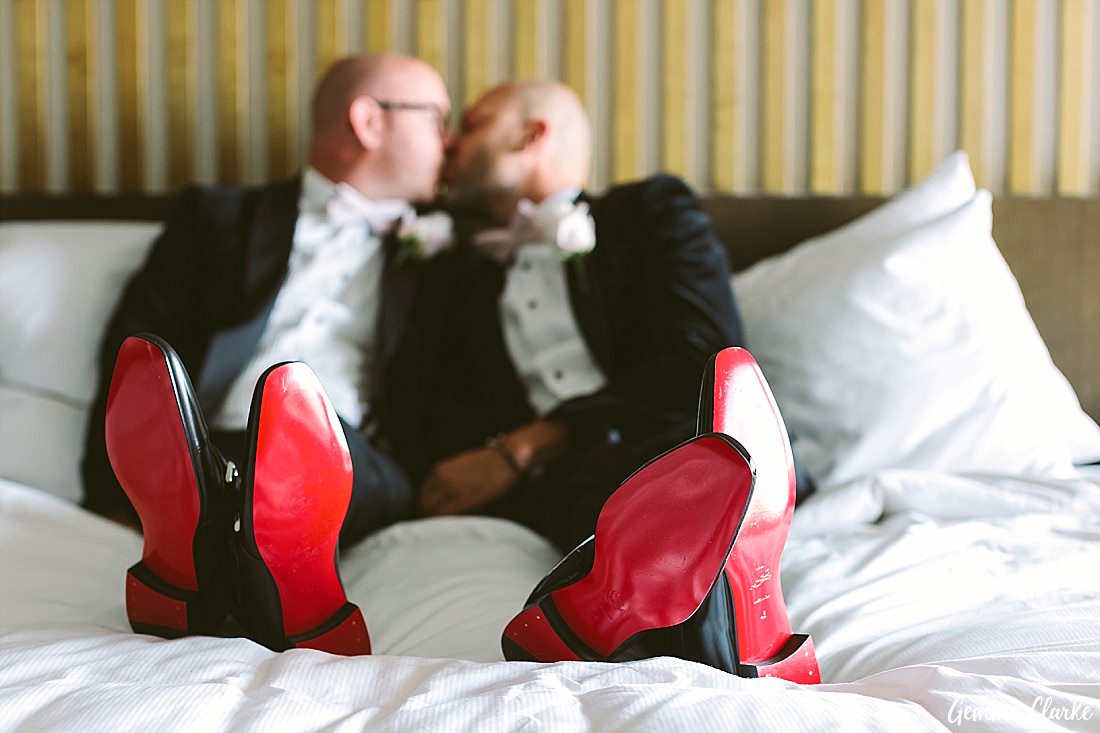 Two grooms sit on a hotel bed with the red soles of their Christian Louboutin shoes at this Sydney Gay Wedding