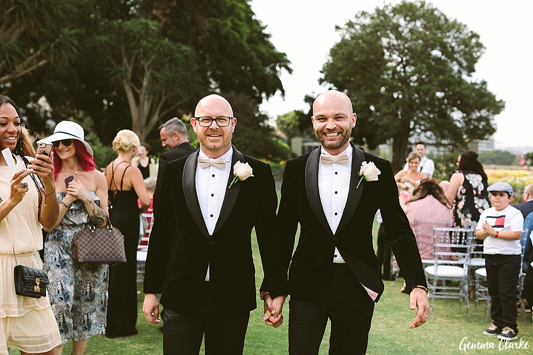 These two grooms walking back down the aisle hand in hand and very happy after their rose garden ceremony at this Sydney Gay Wedding