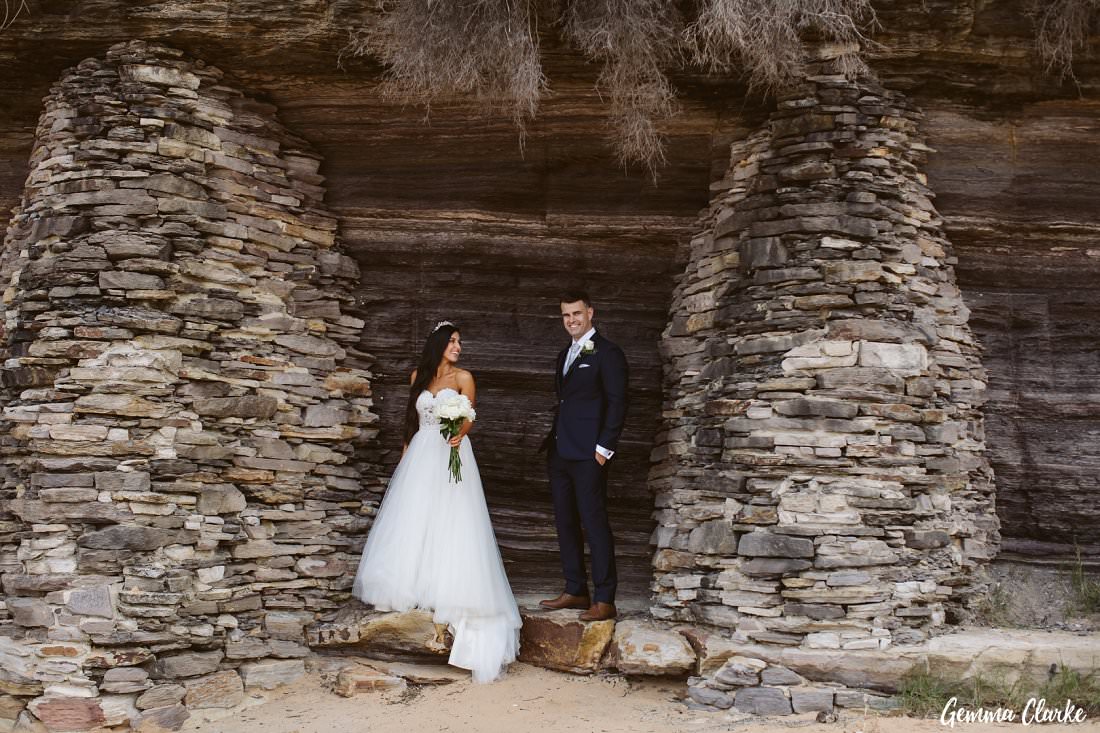Gorgeous bride and groom standing in between gorgeous rock formations at their Bilgola Beach Wedding
